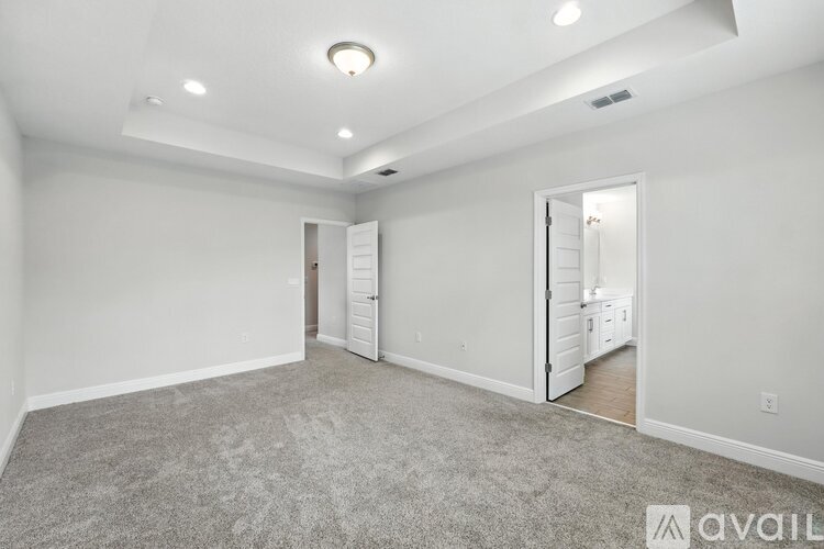 A spacious room with carpeted floor and white walls, with a doorway leading to another room.