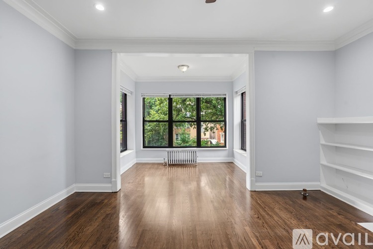 A spacious room with wooden floors and a large window overlooking a balcony.