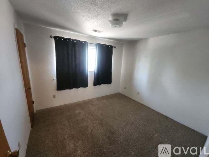 A room with a carpeted floor and a window with black curtains.
