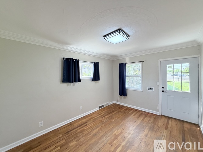 A room with a white door, a window with black curtains, and a wooden floor.