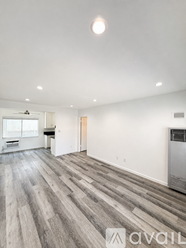 A spacious room with wooden flooring and a refrigerator on the right side.