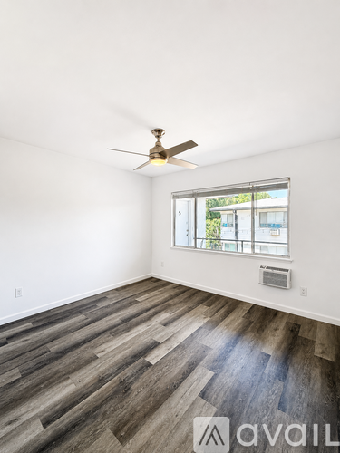 A room with a ceiling fan and a window with a view of trees and a building outside.