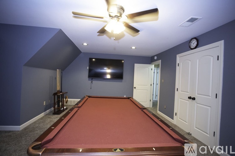 A pool table in a room with a ceiling fan and a clock on the wall.