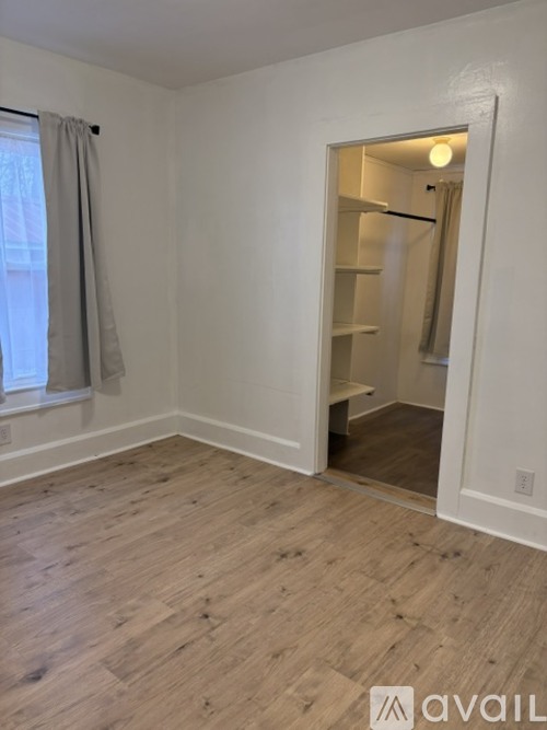 A room with a wooden floor and a white wall with a doorway leading to another room.