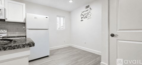A kitchen with white appliances and cabinets, a granite countertop, and a wooden floor.