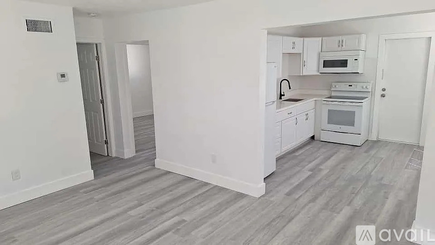 A kitchen with white cabinets and appliances in a room with light wood flooring.