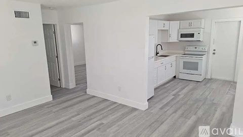 A kitchen with white cabinets and appliances in a room with light wood flooring.