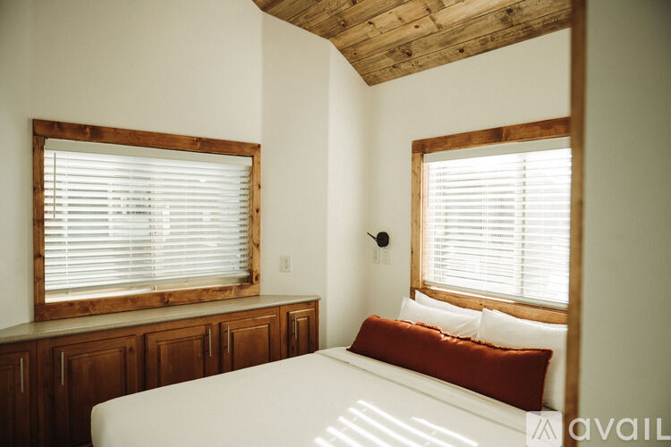 A bedroom with a bed, wooden cabinets, and two windows with blinds.