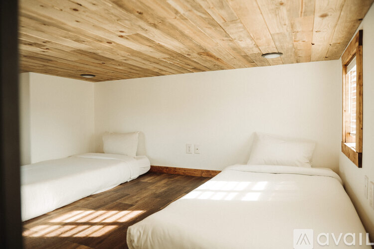 Two white beds in a room with wooden ceiling and a window.
