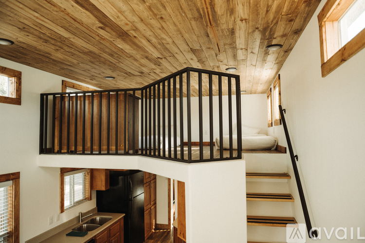 A wooden balcony with black railings is located in the middle of a white room.