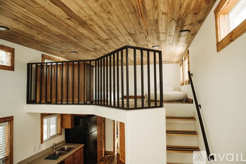 A wooden balcony with black railings is located in the middle of a white room.