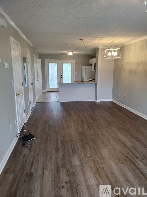 A room with wooden flooring and a kitchen area in the background.