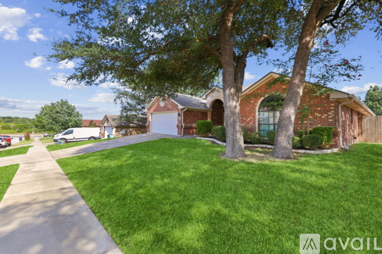 A house with a red brick exterior and a white garage door is surrounded by a well-manicured lawn and trees.