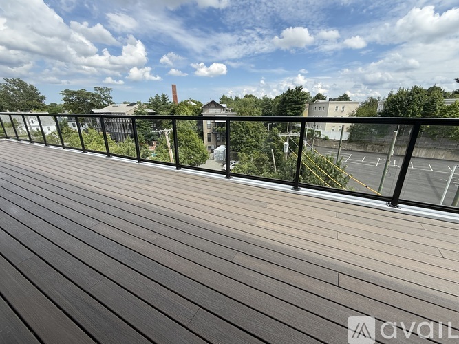 A balcony with a wooden floor and a metal railing overlooking a parking lot and buildings.