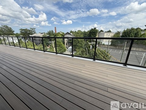 A balcony with a wooden floor and a metal railing overlooking a parking lot and buildings.