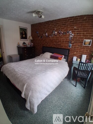 A bedroom with a bed, desk, chair, and a brick wall.