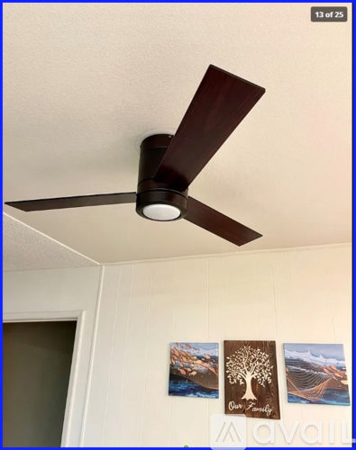 A ceiling fan with a light on, mounted in a room with two pictures on the wall below it.
