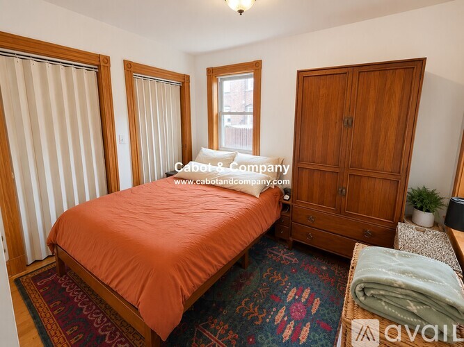 A bedroom with a bed, a cabinet, and a window with blinds.
