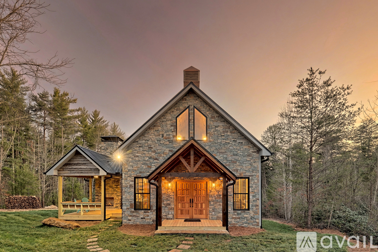 A house with a stone exterior and a wooden door is surrounded by trees.