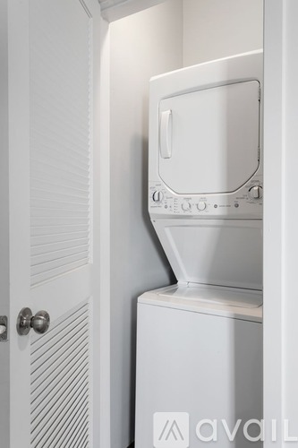 A white washing machine is in a small space between a door and a cabinet.