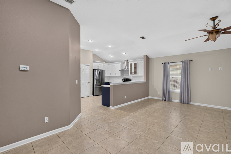 A spacious living room with a ceiling fan and a kitchen area in the background.