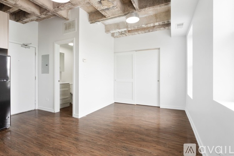 A room with wooden floors and white walls, with a black refrigerator on the left side.