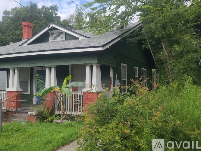 A green house with a porch and a sign that says "AVAIL".