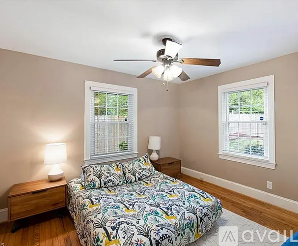 A bedroom with a bed, nightstand, and two windows.