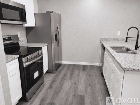 A kitchen with a black stove top oven, a black microwave, a black refrigerator, and a granite countertop.