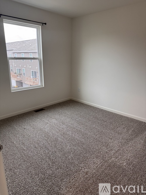 A room with a carpeted floor and a window showing an apartment building outside.