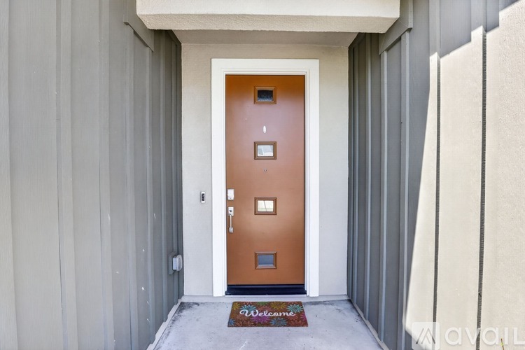 A brown door with a glass window is in the middle of a grey wall.