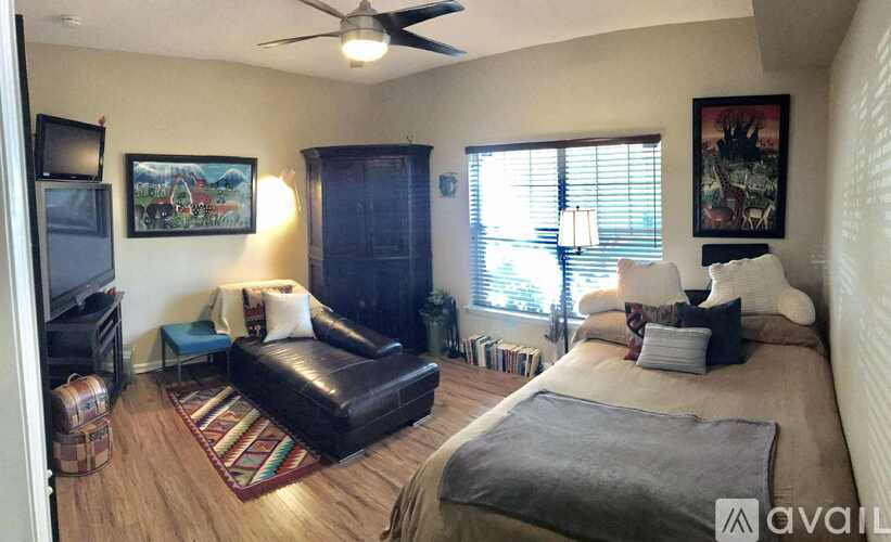 A living room with a black leather couch and a bed with a grey blanket.