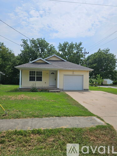 A small house with a garage door is situated in a grassy area.