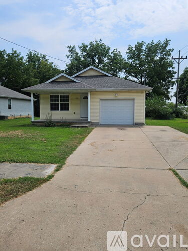 A small house with a garage door is in front of a tree.