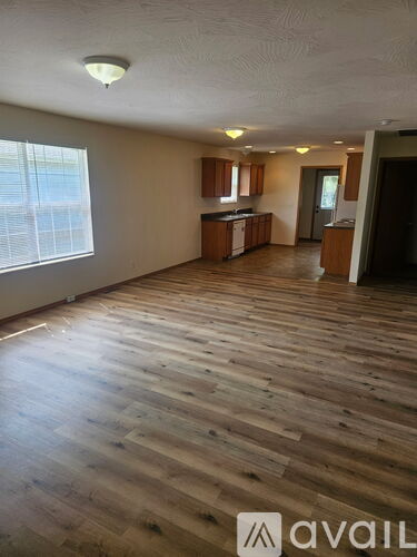 A spacious room with wooden flooring and a kitchen area in the background.