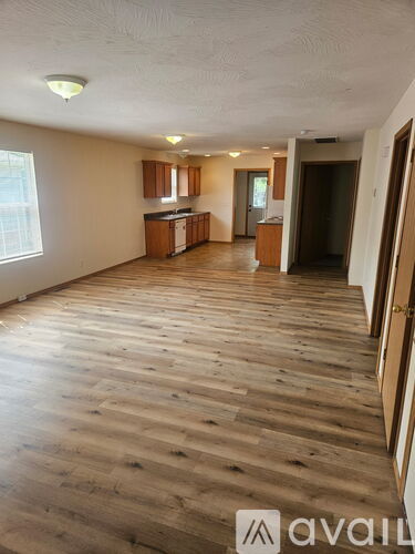 A spacious room with wooden flooring and a kitchen area in the background.