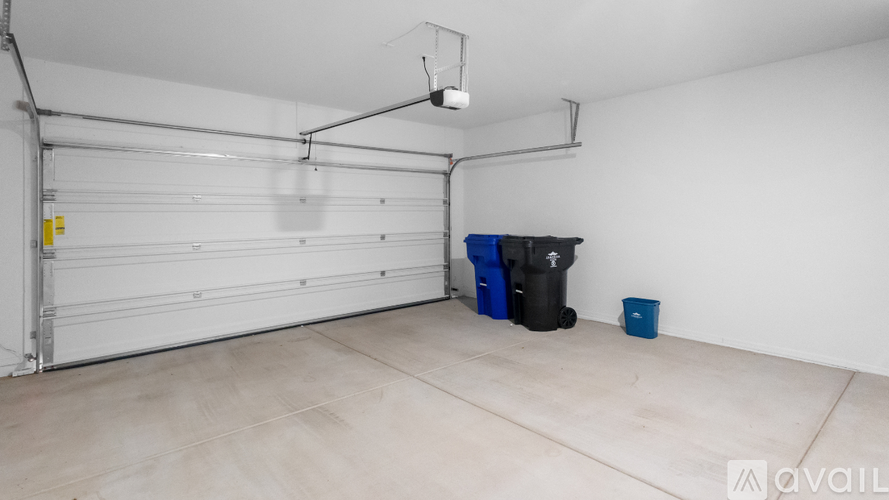 A spacious garage with a white door, a black trash bin, and a blue bucket.