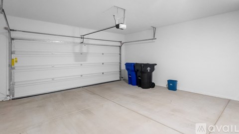 A spacious garage with a white door, a black trash bin, and a blue bucket.