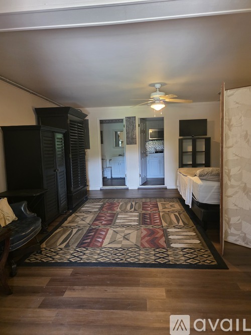 A room with a rug on the floor and a bed with white sheets.