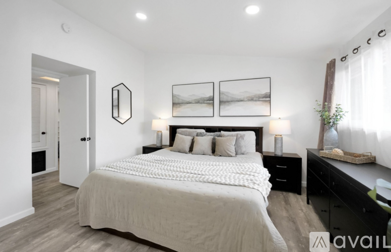 A bedroom with a large bed, two nightstands with lamps, and a mirror above the dresser.