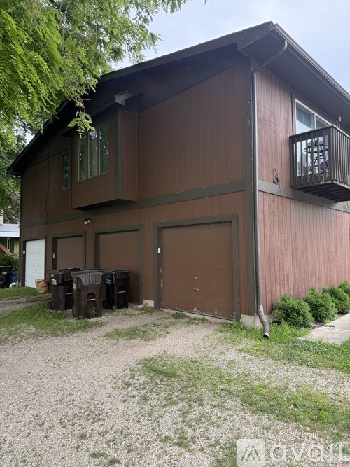 A brown house with a balcony and a gravel driveway.