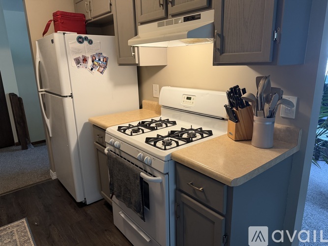 A kitchen with a white gas stove and a white refrigerator with a red cooler on top.
