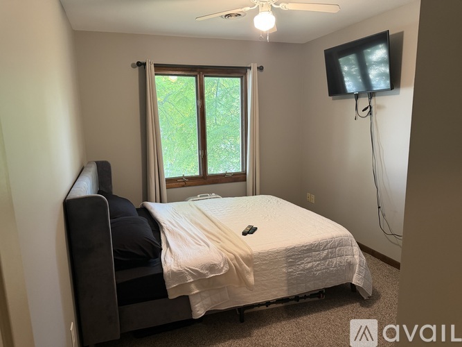 A bedroom with a bed, a ceiling fan, and a flat screen TV mounted on the wall.