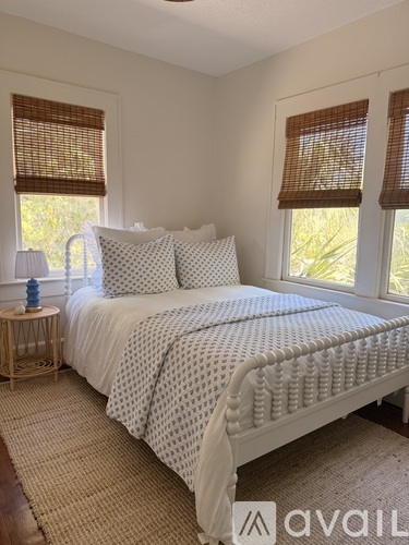 A bedroom with a large bed and a window with brown blinds.