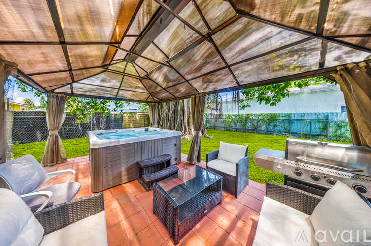 A patio with a hot tub and a grill under a canopy.