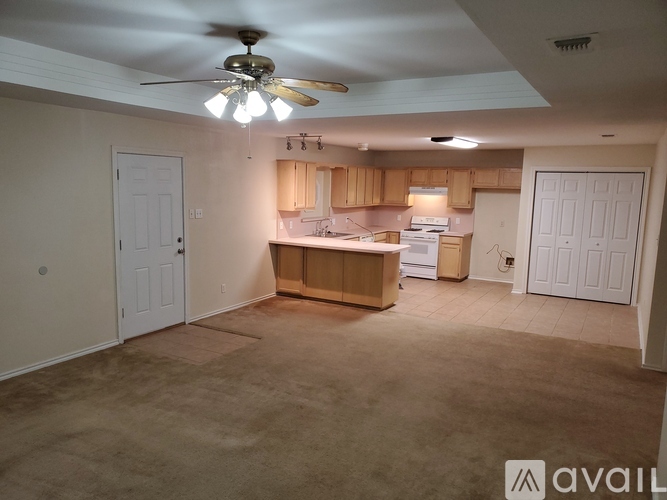 A room with a ceiling fan and a kitchenette in the background.