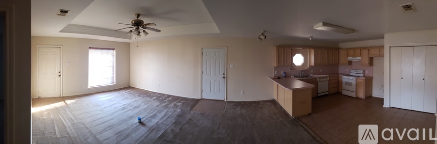 A room with a ceiling fan and a kitchen area in the background.
