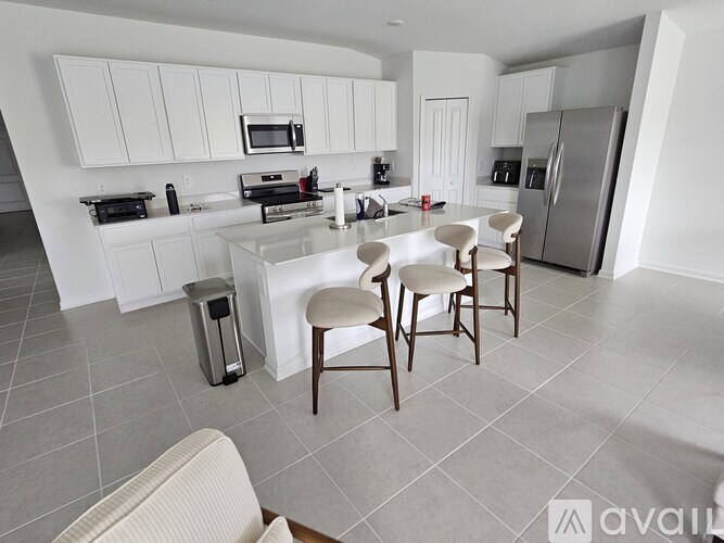 A kitchen with white cabinets and a white island with four chairs around it.