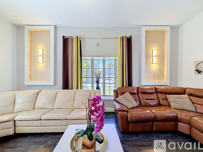 A living room with a white and brown leather couch, a coffee table with flowers, and a window with curtains.
