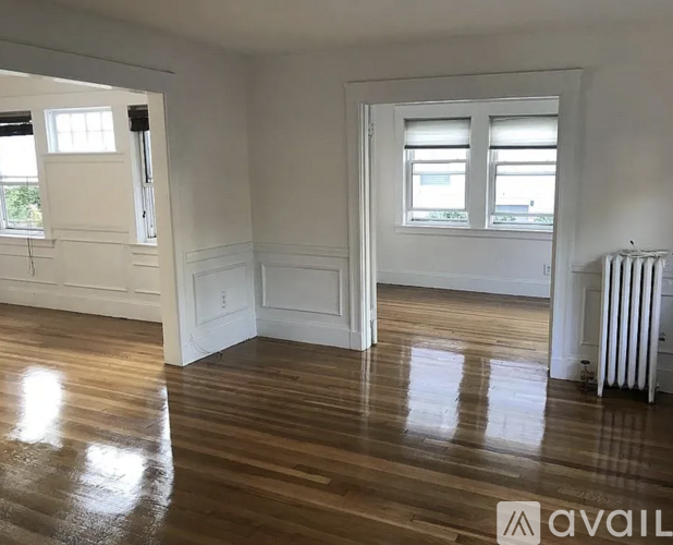 A room with wooden floors and white walls, with a window and a radiator visible.